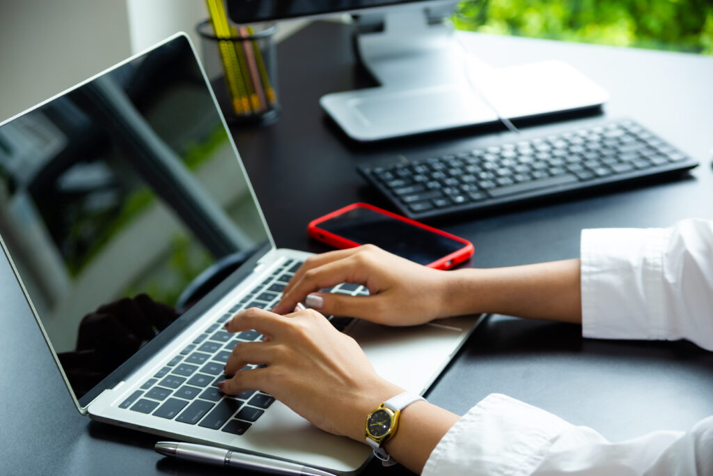 Female hands typing on a laptop keyboard in a dimly lit workspace